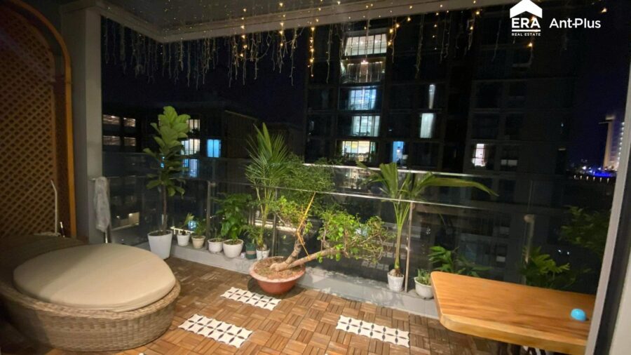Ban công lát gỗ nhiều chậu cây và đèn dây buổi tối căn hộ Linden